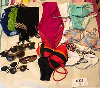 Overview photo of all swimwear pieces laid out including bikinis, one-piece swimsuits, sarongs, and sunglasses