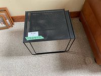 Large black metal nesting table with mesh top and tubular legs, sitting on carpeted floor next to leather couch.