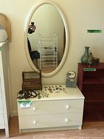 Photo showing dresser and oval mirror mounted on wall, items arranged with jewelry boxes and decor on dresser surface.