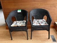 Front view of two black wicker chairs with patterned cushions, placed side by side on a wooden floor.