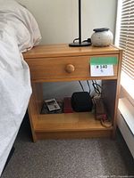 Wood nightstand showing side view with lower shelf and drawer, lamp and ceramic vase on top.