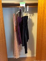 Three dresses hanging in a closet on hangers. Visible wall and wooden closet rod.
