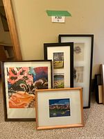 Four framed art prints leaning against a wall on carpet - shows a floral abstract print, a triptych of landscape prints, a photographic detailed print, and a framed cityscape print.