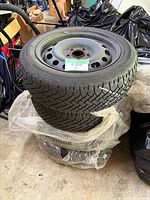 Four stacked winter tires mounted on steel rims with plastic protective bag and lot label