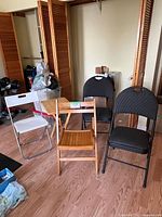 Set of four folding chairs and one folding wood table arranged in a room with a wooden floor, showing different styles and materials.