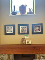 Three framed art prints by Roy Henry Vickers displayed on the wall with two Indigenous decorative items below and pottery on shelf above.