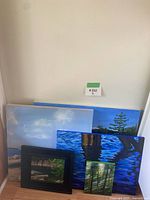 Five PNW inspired acrylic paintings stacked leaning against wall, showing different nature scenes including sky, trees, water, and forest.