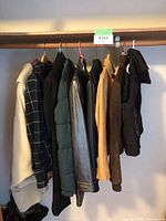 Nine women's jackets and coats hanging on hangers in a closet, visible are various colors and materials including leather, suede, wool, puffer styles