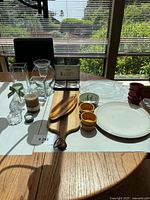 Overview of assorted kitchenware and serveware items including glass vases, silver plated cheese cutter set, ceramic bowls and plates, wooden cutting board, and decorative items.