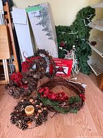 Boxed artificial Christmas tree parts, multiple pinecone and ribbon decorated wreaths, and tangled string lights on floor