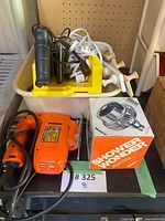 Orange Black & Decker jigsaw with cord, Stanley miter saw parts in yellow bucket, Shower Wonder box on shelf
