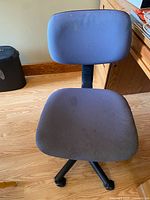 Front view of the gray desk chair showing fabric seat and backrest, on wooden floor near wooden desk.
