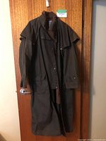 Front view of long brown oilskin coat with buttons and flap pockets hung on door.