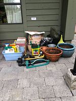 Full view of garden pots, tools, and supplies placed on patio against wall.