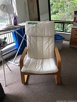 Front view of IKEA Poang chair showing beige seat cushion and padded headrest with visible stitching and wooden armrests.
