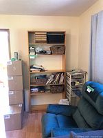 Full view of the large wood bookshelf with five shelves against a beige wall. Shelves contain storage baskets and small items, but content not included in sale.