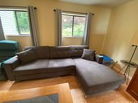 Wide angle view of large dark grey fabric couch with chaise on right side, including one throw pillow placed on the left couch arm.