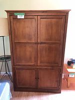 Front view of large wooden media cabinet with two upper and two lower paneled sliding doors, wooden knobs, medium wood tone.