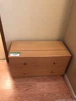 Front view of the low pine dresser showing two drawers with wooden knobs and flat top surface against a beige wall and wood floor.