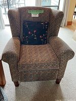 Front view of recliner armchair showing geometric upholstery, wingback design, and floral pillow.