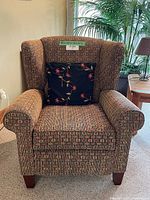 Front view of the manual recliner chair upholstered in patterned fabric with a floral decorative pillow placed in the seat area.