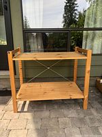 Side view of the wooden garden station showing two shelves and frame with cross braces.