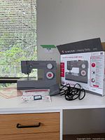 Front view showing sewing machine with original box, foot pedal, instruction manual and accessories on table