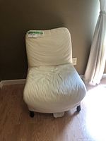 Front view of cream-white slipcovered accent chair showing gently curved backrest, seat, and two black feet.