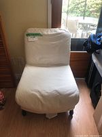 White slipcovered accent chair positioned in front of glass door; shows full front view of the chair including cushioned back and seat.