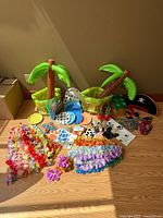 Wide view of all tropical party decorations laid out on floor including leis, inflatable palm trees, pirate eye patch, and themed plates and cups.