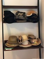 Two shelves displaying an assortment of vintage hats including felt hats, woven straw hats, and structured helmets in neutral colors.