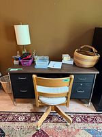 Front view of vintage metal desk with faux wood top and wooden swivel chair in front. The desk has six black metal drawers and silver handles.