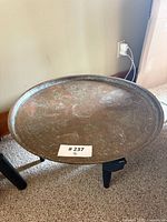 Copper tray table set placed on carpeted floor, showing copper tray on black base stand from a side angle.