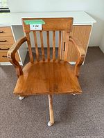 Front view of vintage wooden office chair with armrests, vertical slats on the backrest, and mounted on caster wheels, placed on carpet.