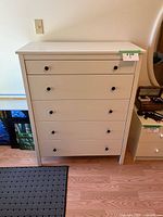 Front view of white 5-drawer dresser showing five drawers with black knobs and flat top.