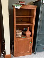 Wood storage unit with decorative items inside including a basket and vase, showing the whole unit in context between walls and furniture.