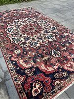 Full view of the rectangular Bakhtiari rug laid out showing central medallion and floral motifs with red, blue, ivory colors.