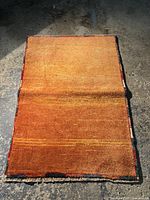Full view of rectangular orange rug laid on concrete