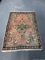 Full view of a small rectangular rug with pink and black tones, floral patterns, and a central medallion.