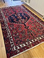 Overall view of rug on wood floor, showing full pattern and fringes