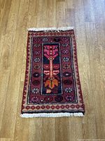 Full view of the small rectangular Persian rug laid on a wooden floor, showing typical Persian style patterns with natural color wool and fringed edges.