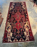 Full view of rectangular vintage handmade Persian rug with dominant red, cream, blue, and black geometric patterns and medallion motifs.