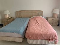 Two single beds side by side with blue and pink blankets. Light wood headboards and base frames on wheels visible.