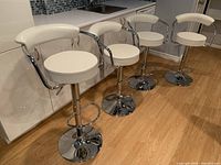 Four white faux leather and chrome bar stools lined up in front of a counter