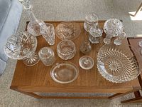 Overview of assorted crystal items on wooden table, including decanter, bowls, jars, glasses with intricate cut patterns.