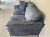 Side view of the blue suede loveseat showing the armrest and back cushions.