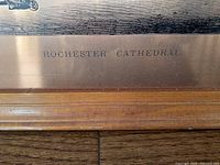 Close-up photo showing the etched brass plate with inscription 'ROCHESTER CATHEDRAL' above the wooden frame edge.