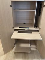 Front view with cabinet doors open showing shelf inside, sliding keyboard tray extended, and a lower flat sliding drawer, light wood finish cabinet.