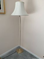 Full view of tall brass floor lamp with white fabric shade in room corner