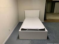 Full view of assembled white single bed frame with mattress and headboard inside a room with carpet.